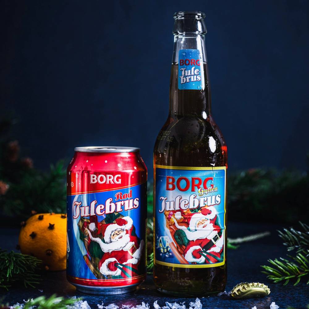 En flaske og en boks med julebrus fra Borg, pyntet med juledekorasjoner og snø rundt på bordet.