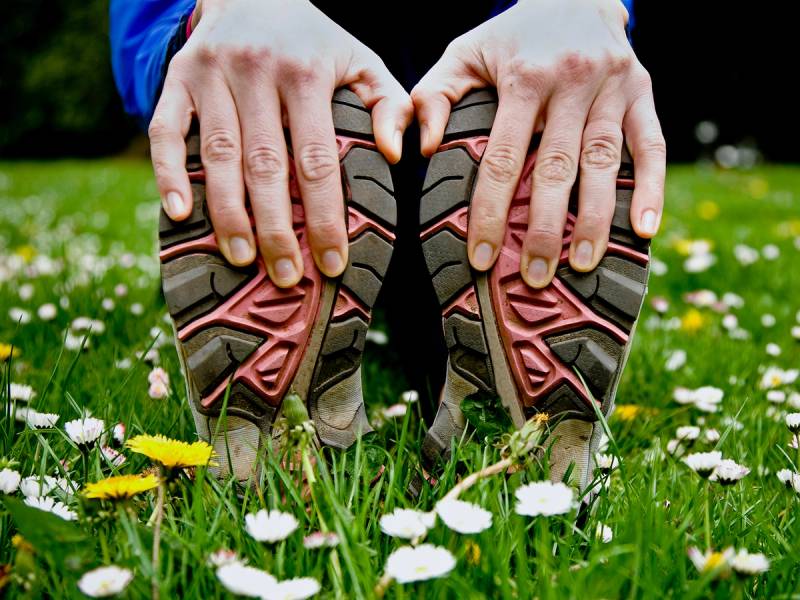 To personer holder opp et par tøyhoder som er formet som sko, med en grønn plener og blomster i bakgrunnen.