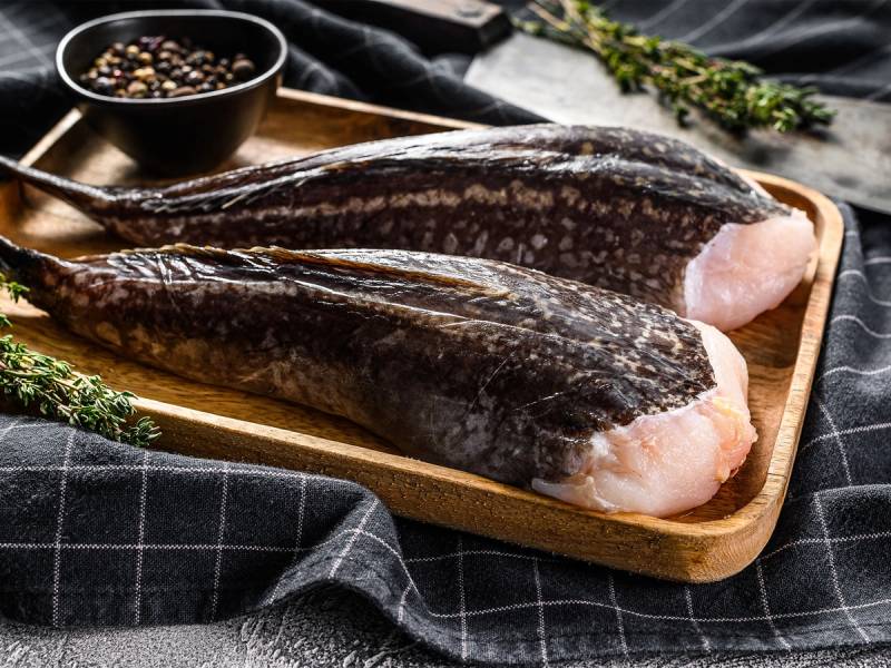 To breiflabb-halser på et treplatet med krydder og urter rundt, klar til tilberedning.