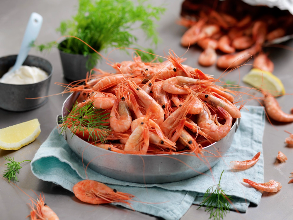 Røde reker på et fat med sitronbåter og dill, klar til servering.
