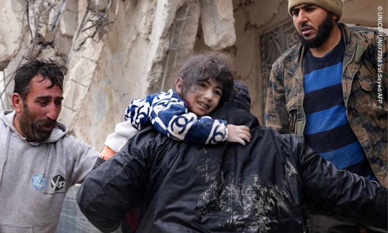 En gruppe mennesker samles rundt en person som får hjelp, med en steinvegg i bakgrunnen, sannsynligvis i Syria eller Tyrkia.