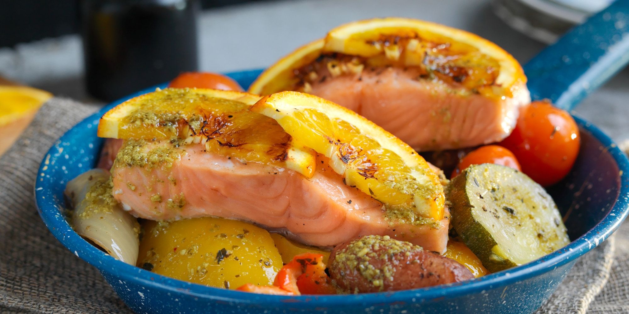 Laksefilet med ovnsbakte grønnsaker som poteter, cherrytomater og gulrøtter på en blå tallerken.