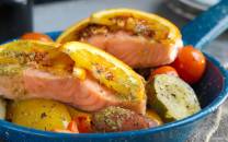 Laksefilet med ovnsbakte grønnsaker som poteter, cherrytomater og gulrøtter på en blå tallerken.