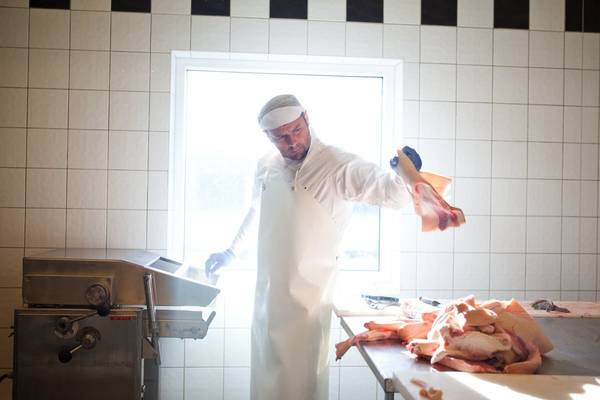 En person i hvit kjeledress står foran et vindu i et rom med hvite fliser, og holder opp en dukke eller et kosedyr i hånden.