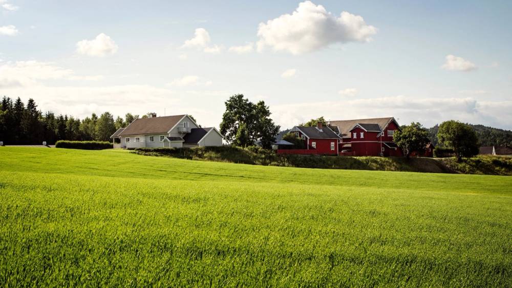 Grønt jorde med gårdshus og låver i bakgrunnen.
