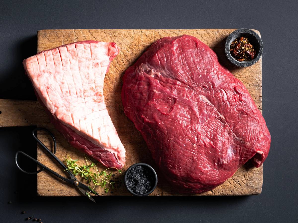 Et stykke angus tritip kjøtt og en morbrad på et skjærebrett med krydder og urter.