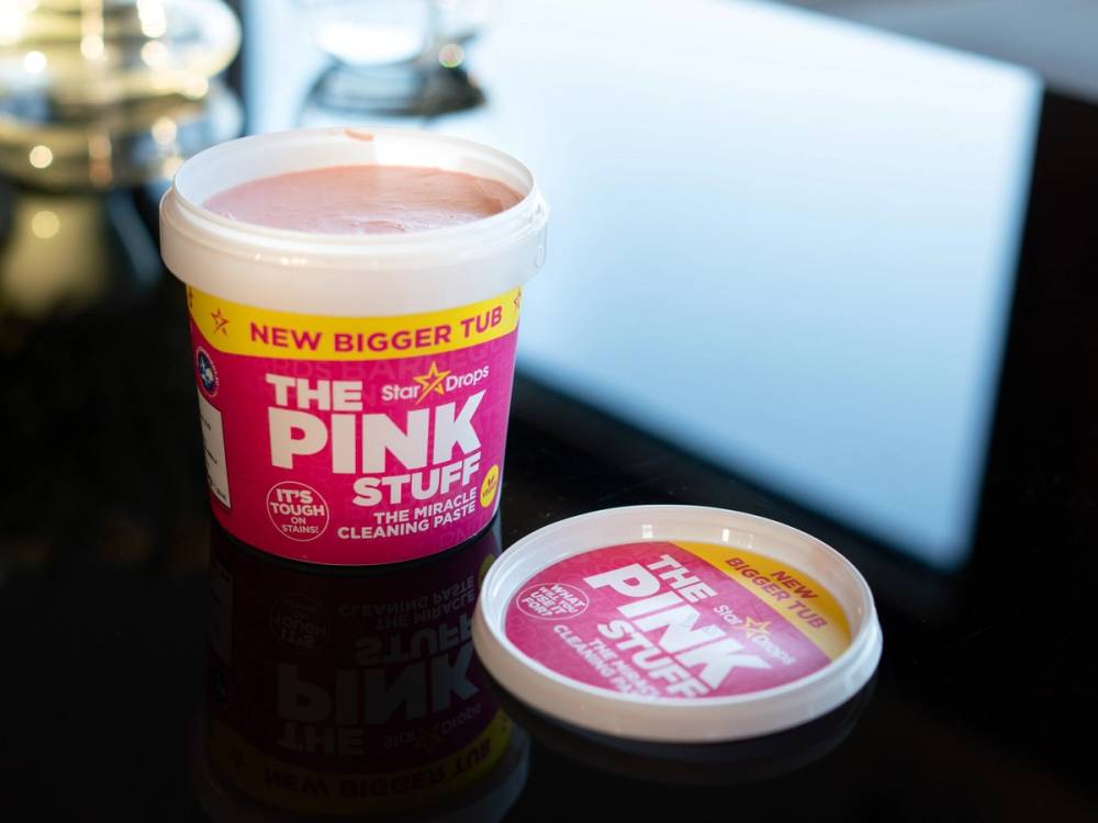En bøtte med rosa rengjøringskrem kalt The Pink Stuff står på et bord, med en annen liten beholder med samme navn ved siden av.