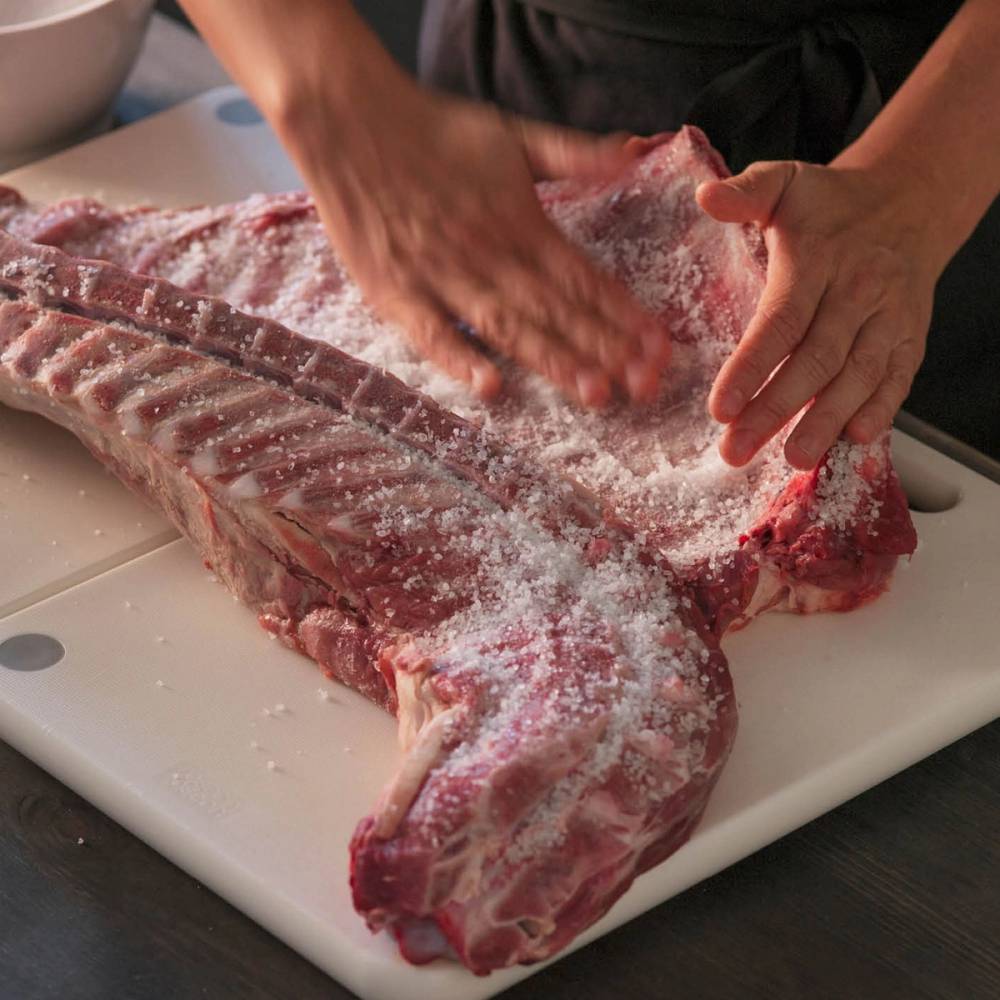 Person som salter og forbereder pinnekjøtt på skjærebrett.