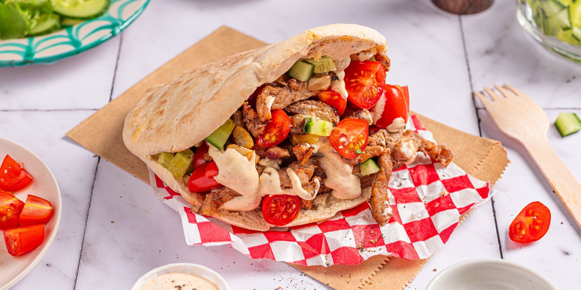 Kebab med strimlet lam, tomater og grønnsaker i pitabrød på et bord.