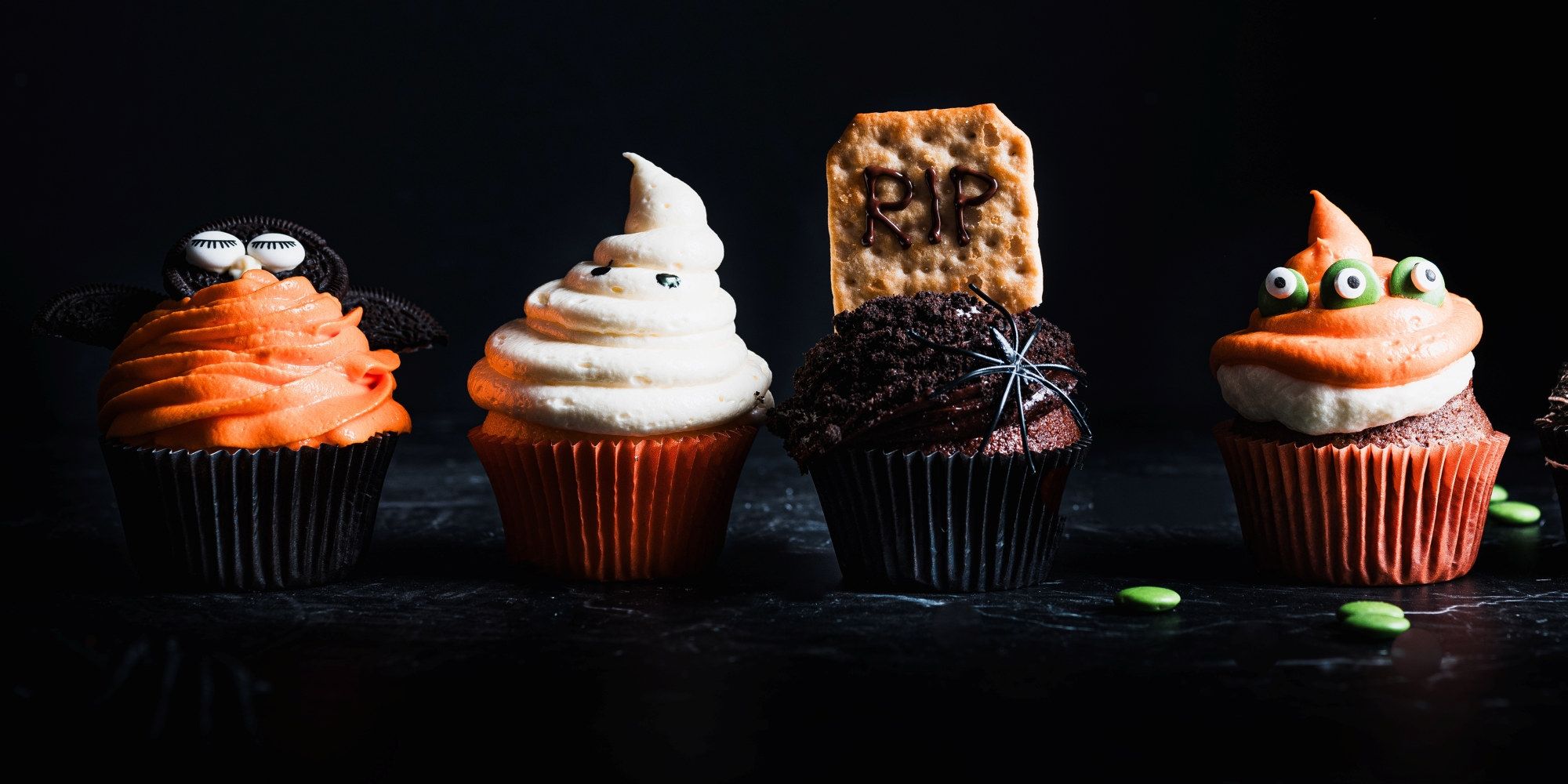 Fire cupcakes med halloween-tema dekorasjoner på en svart bakgrunn.