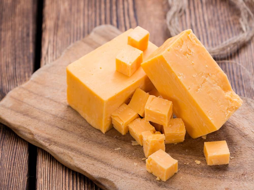 Ulike biter av gul ost på en treplate, med en rustikk trebakgrunn.
