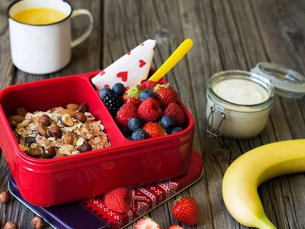 En matpakke med granola, bær og en banan på et bord, klar til å lages av barn.