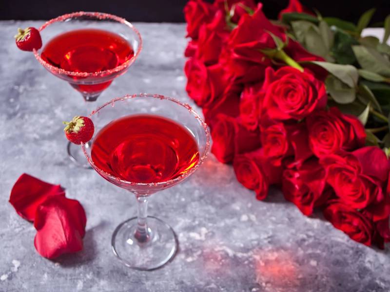 To romantiske cocktailglass med rødt innhold og en bukett røde roser, sannsynligvis for Valentinsdag
