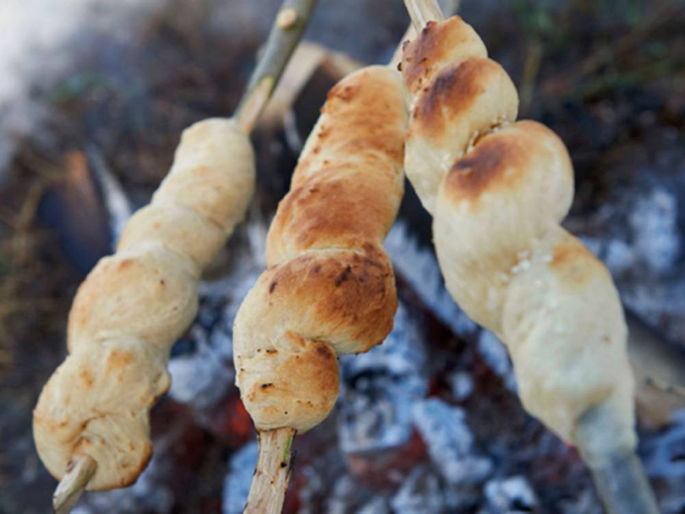Pinnebrød stekes over åpen ild på spyd, med glovarme brød som er delvis ferdigstekte.