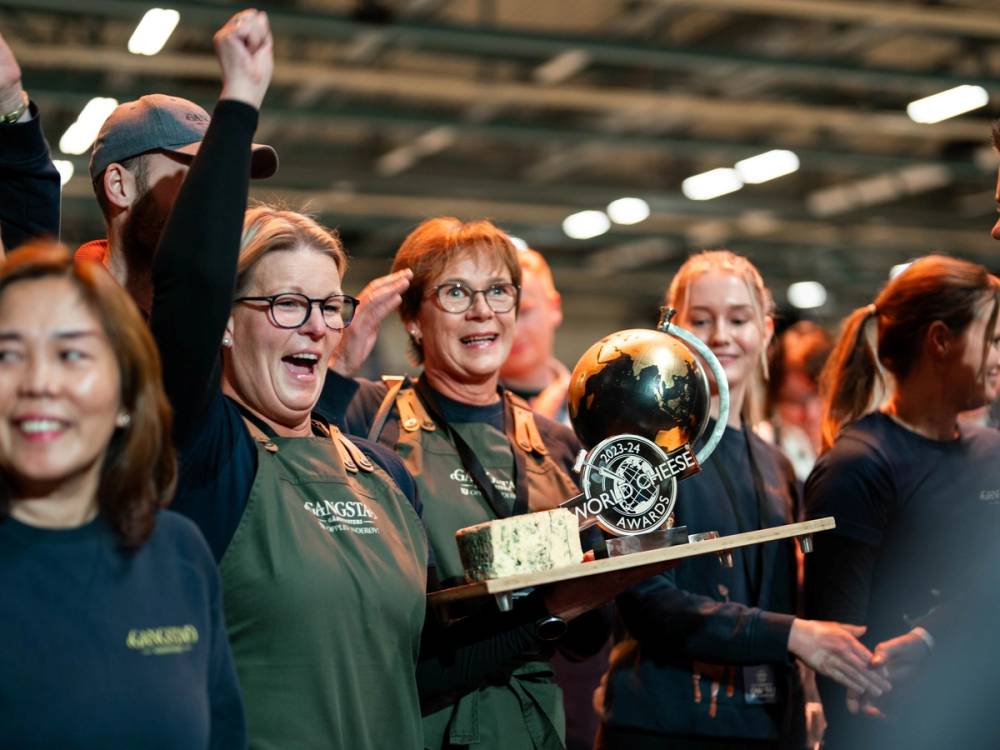 En gruppe mennesker feirer med en pokal og en sjokoladekake på en innendørs arena, sannsynligvis etter en konkurranse eller arrangement.