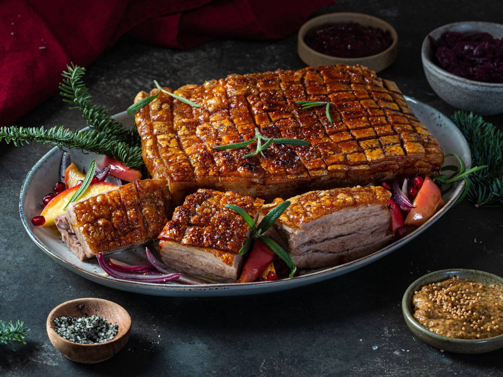 Ribbe med sprø svor på et fat, pyntet med grønne urter og serveringsfargerike tilbehør.