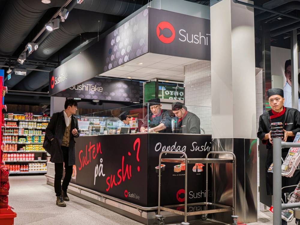 En sushi-stand i Oslo City med ansatte som serverer kunder, og en kunde som står foran disken.