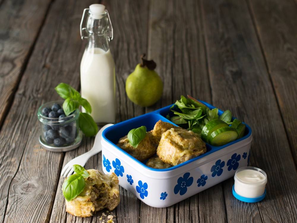 Pizzasnurrer på et fat med tilbehør som agurk, avokado og en liten skål med yoghurt, med melk og en pære i bakgrunnen.