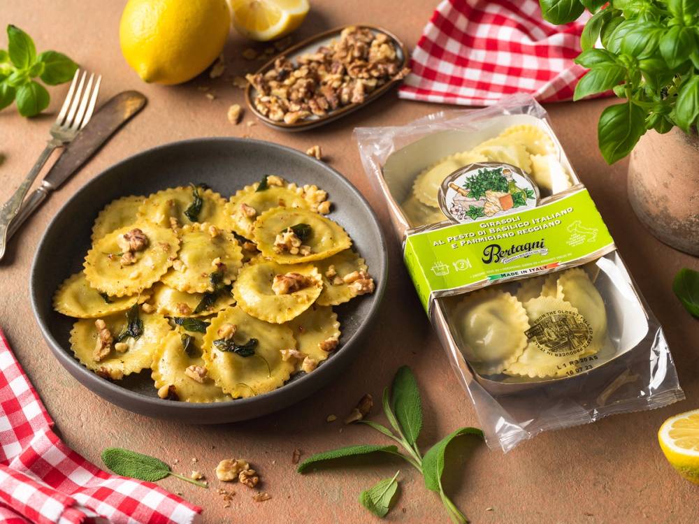 Ferdigkokt pasta med nøtter og sopp i en svart bolle, omgitt av sitroner, urter og en pakke med pasta på et kjøkkenbord.