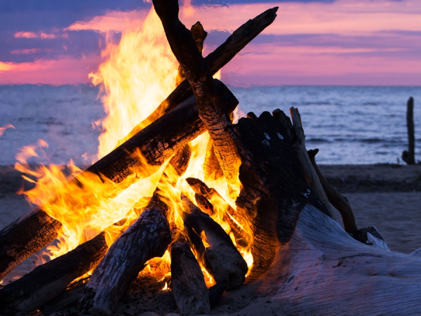 Bål med store flammer på en strand under solnedgang, feiring av sankthans.