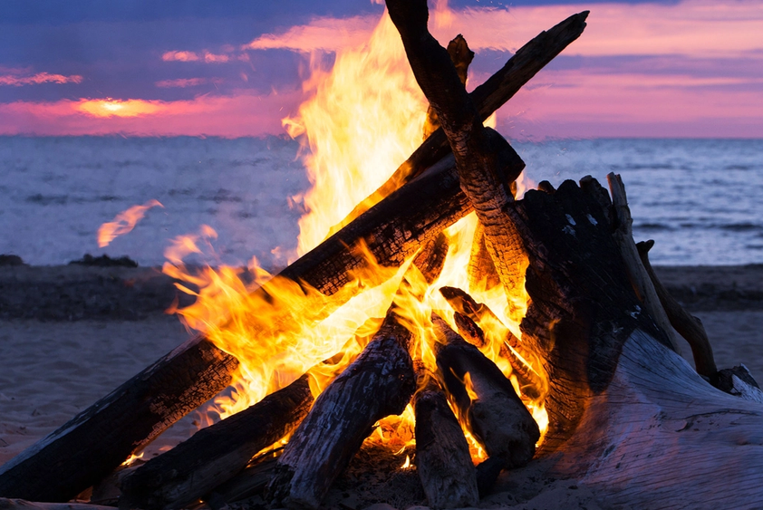Bål med store flammer på en strand under solnedgang, feiring av sankthans.