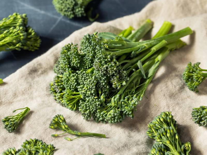 Ferske broccolibuketter liggende på et kjøkkenhåndkle med noen små blomsterbuketter rundt