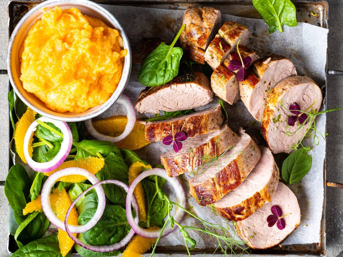 Svinefilet skåret i skiver med grønnsaker og en liten bolle med potetmos på et fat.