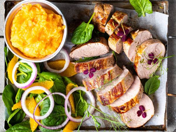 Svinefilet skåret i skiver med grønnsaker og en liten bolle med potetmos på et fat.