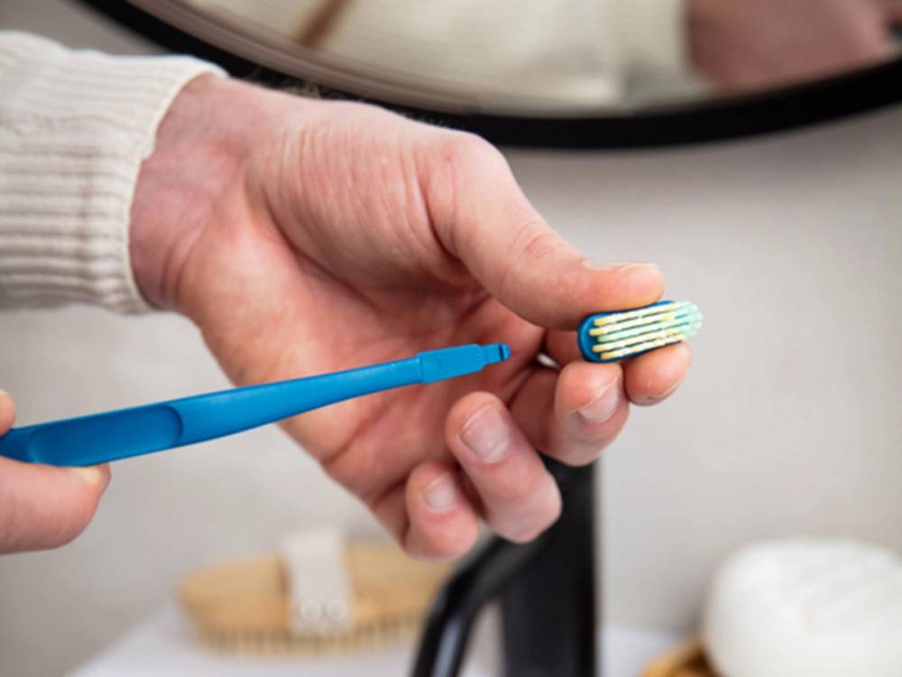 En person holder en Jordan-børste og viser den frem, mens de rengjør tenner med en blå tannbørste.