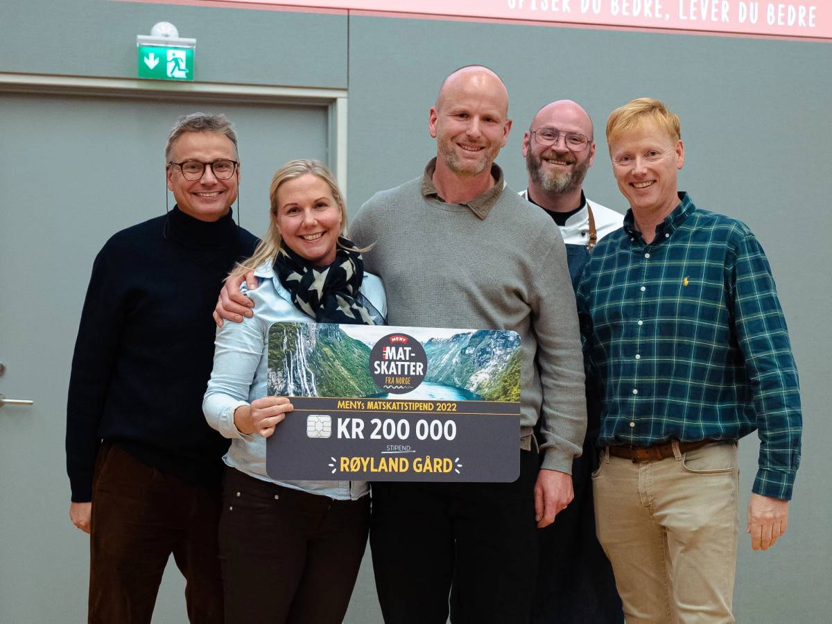 Gruppemedlemmer holder opp et stort sjekk med teksten 'Matskattstipendet 2022' og beløpet 200 000 kroner, foran en blå vegg.