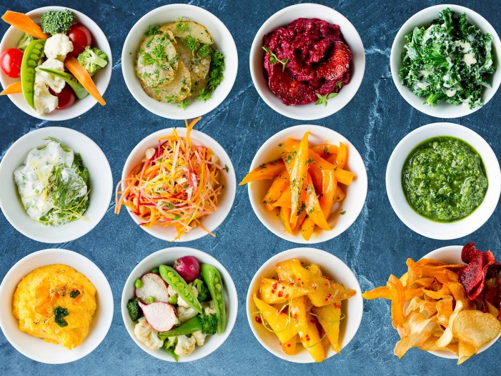 Et utvalg av små tallerkener med høstlige tapasretter som grønnsaker, dipper og salater på et blått bord