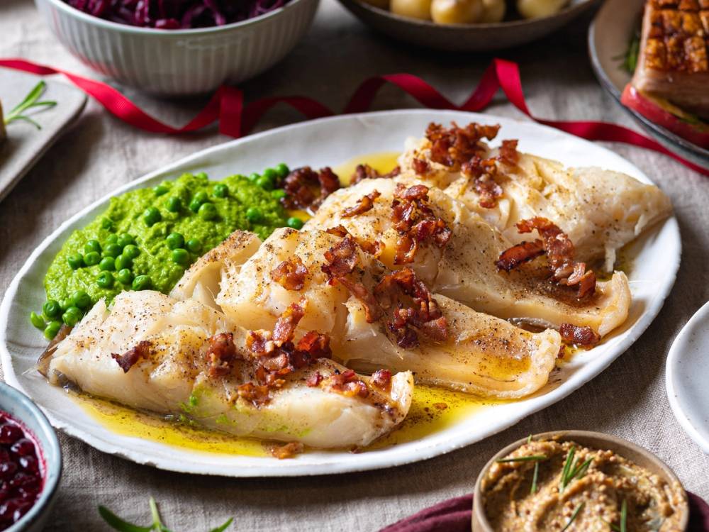 Stekt torsk med bacon og grønnsaker på en hvit tallerken, omgitt av juledekorasjoner.