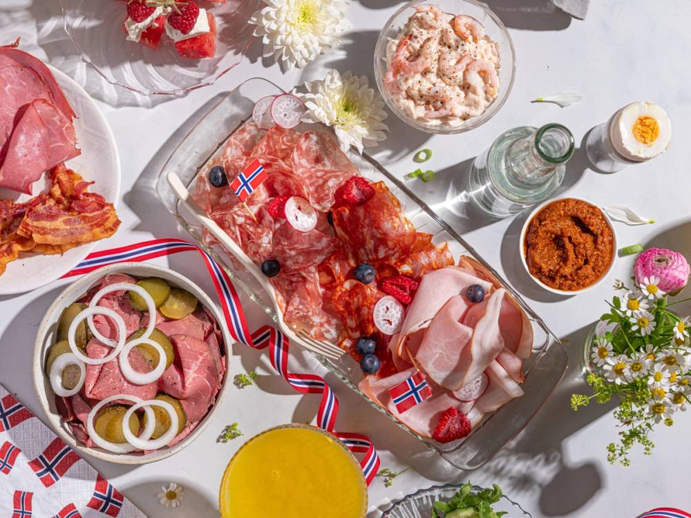 Frokostbord med norske flagg, pølser, kaker og blomster til 17. mai-feiring