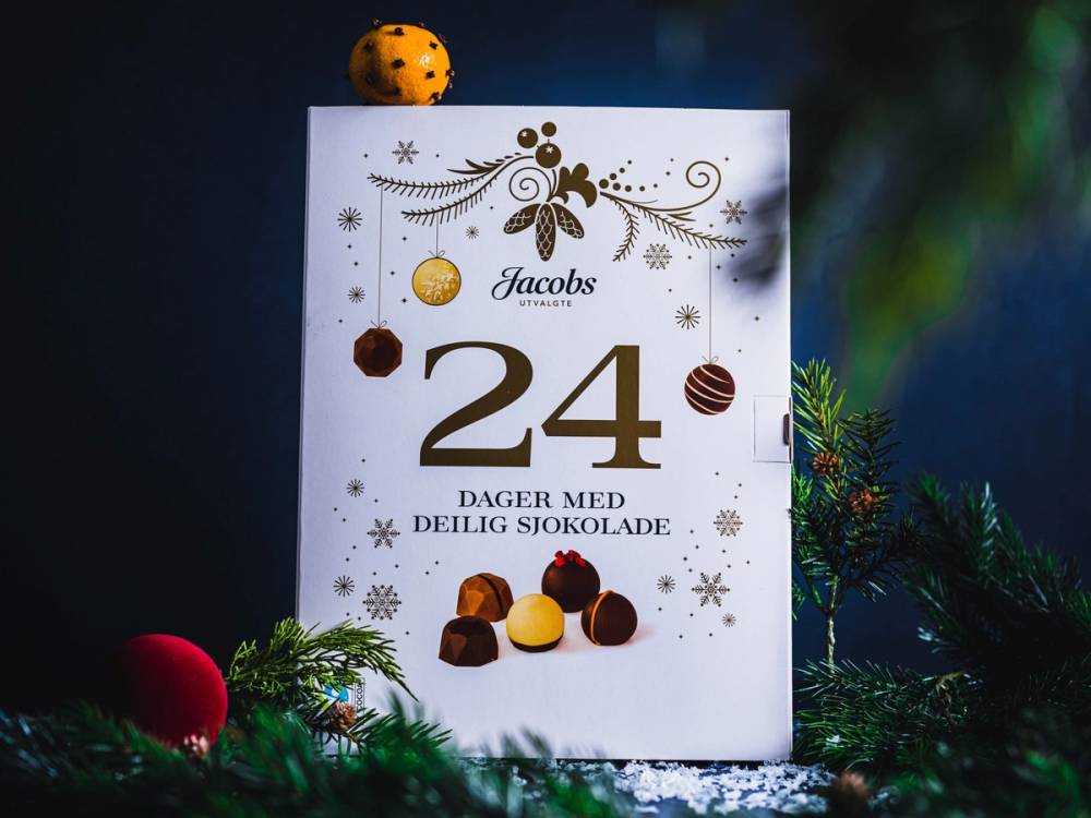 En kalender for 2022-2024 med juledelementer og sjokolade på forsiden, plassert blant julegrener og pynt.