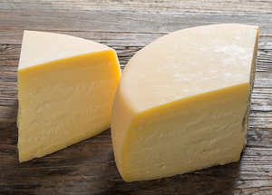 To stykker gul ost på en treplate, med en glatt overflate og litt tekstur på kantene.
