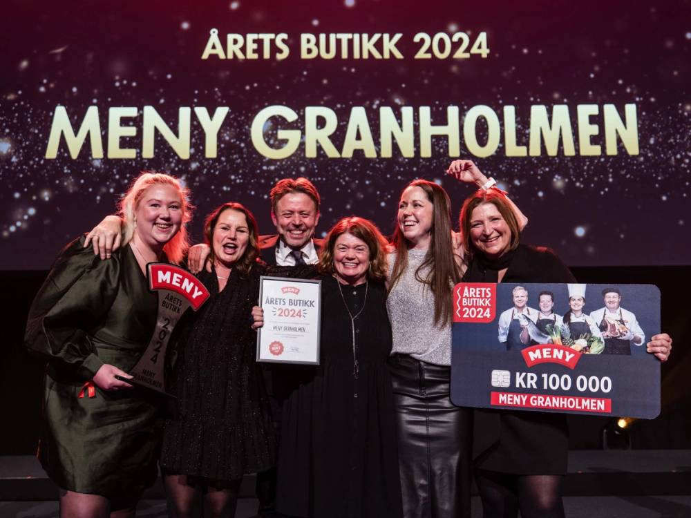 Fem personer står på scenen med en stor sjekk og et banner for Meny Granholmen, feirer en prisutdeling i 2024, med stjerner og festlige lys i bakgrunnen.