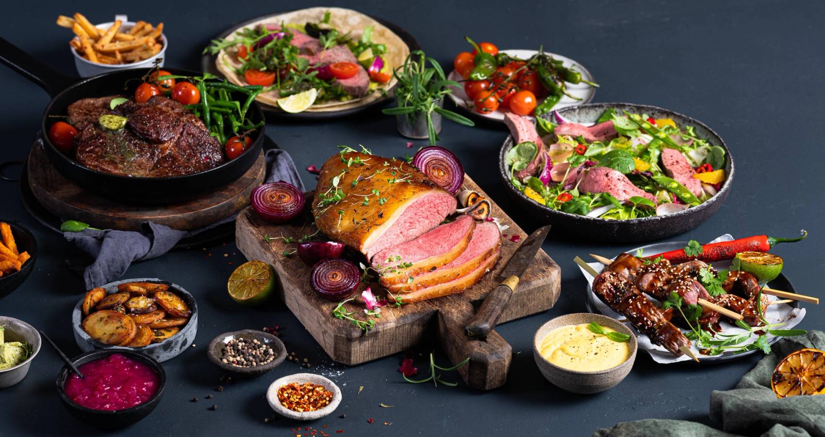 Et bord med ulike retter av biff, salater og tilbehør, klar for helgemiddag.