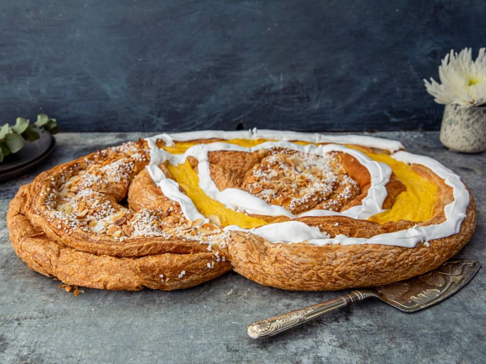 To wienerkringle med sukker og fyll, servert på en tallerken med en skje ved siden av, mot en mørk bakgrunn.