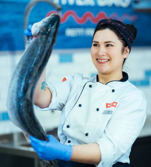En person i kokkeuniform holder opp en stor fisk i en fiskebutikk eller på en fiskemesse.