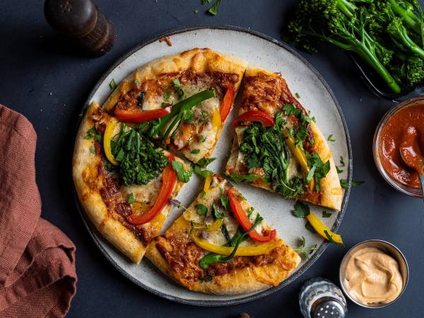 Pizza med broccolini, paprika og ost på en rund tallerken