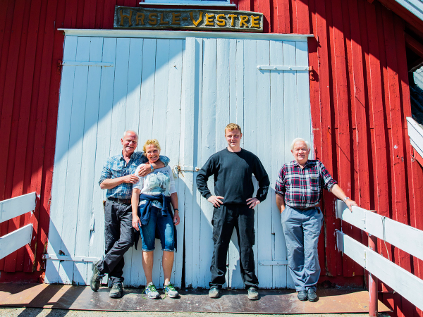 Fire personer står foran en stor, blå dør på en rød bygning med skiltet 'Hasle Vestre'.