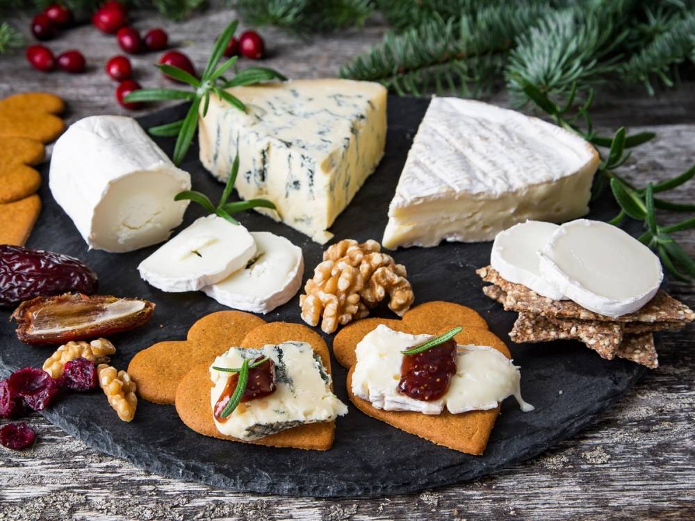 Ulike typer ost på et serveringsfat med juledekorasjoner i bakgrunnen.