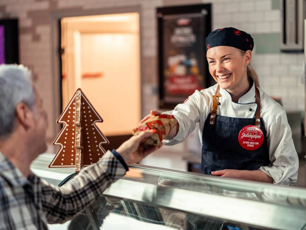 Kvinne i klesbutikk som hjelper en kunde med å prøve klær, med en julepyntet dekorasjon i bakgrunnen.