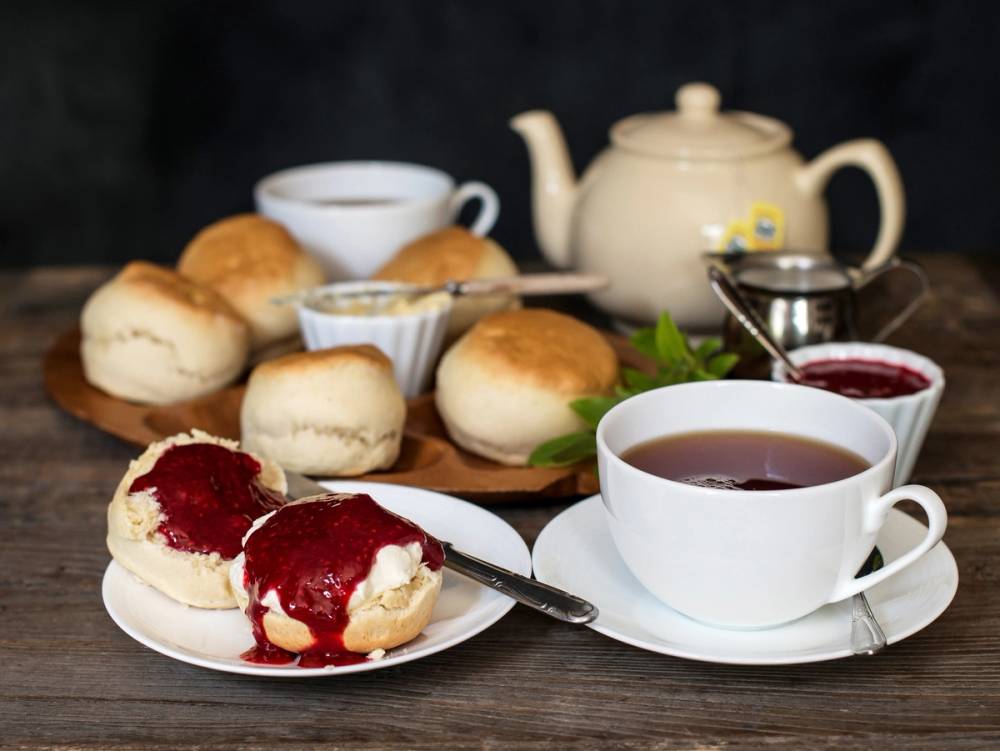 Scones med jordbærsyltetøy og en kopp te på et bord med en tekanne og en liten skål med syltetøy