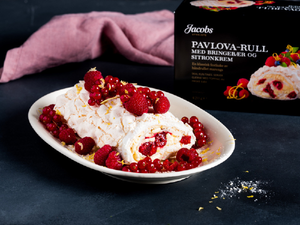 Pavlovarull med bringebær og sitronkrem på en hvit tallerken, med en pakke av Pavlova-Rull i bakgrunnen.
