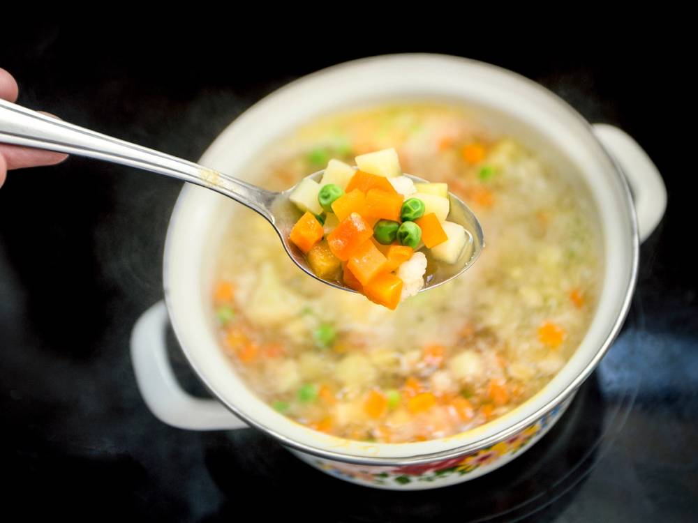 Sølvskje med fryste grønnsaker som helles opp i en kjele med grønnsakssuppe