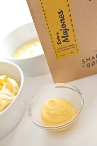 Kremet majones i en liten glasskål med en større bolle med majones i bakgrunnen og en papirkasse med majones på siden