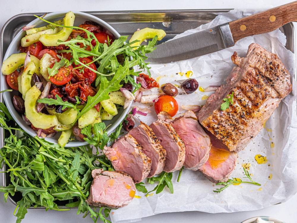 Svinefilet med tatziki og en grønn salat med cherrytomater, servert på et fat med et kjøttstykke skåret opp.