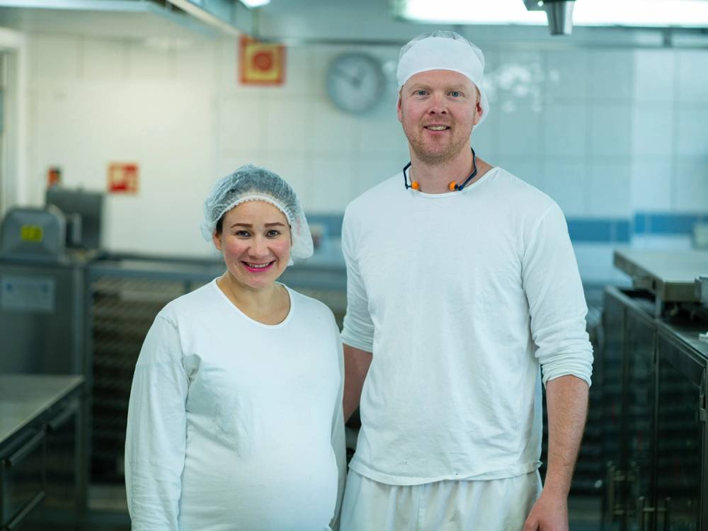 To personer står i en fabrikk, sannsynligvis produsenter i Mexico, med industrielle maskiner i bakgrunnen.