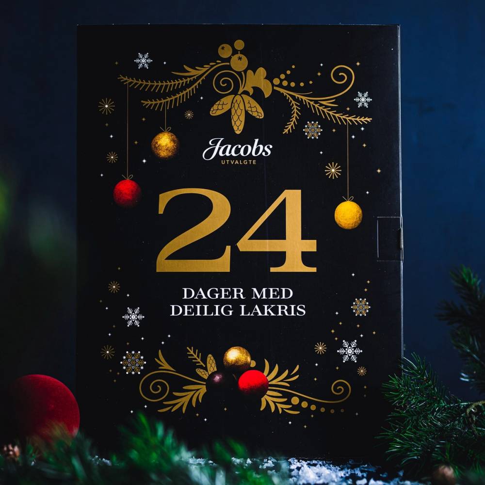 En julekalender med nummer 24 og teksten 'Dager med deilig lakris' på forsiden, dekorert med gull- og røde julekuler og julegrener.
